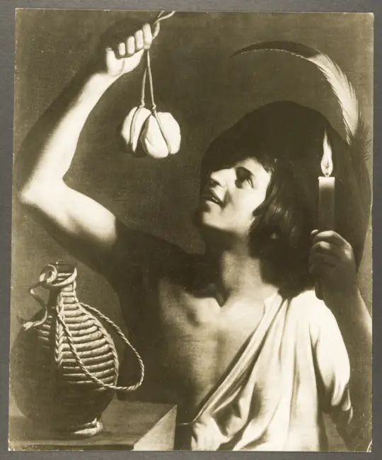 Giovane uomo con in mano una candela accesa che solleva un formaggio e un fiasco posato di lato